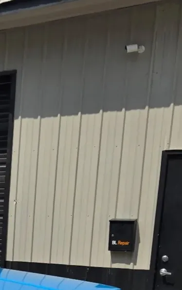 The front door of BL Repair with the black BL Repair drop box on the steel siding